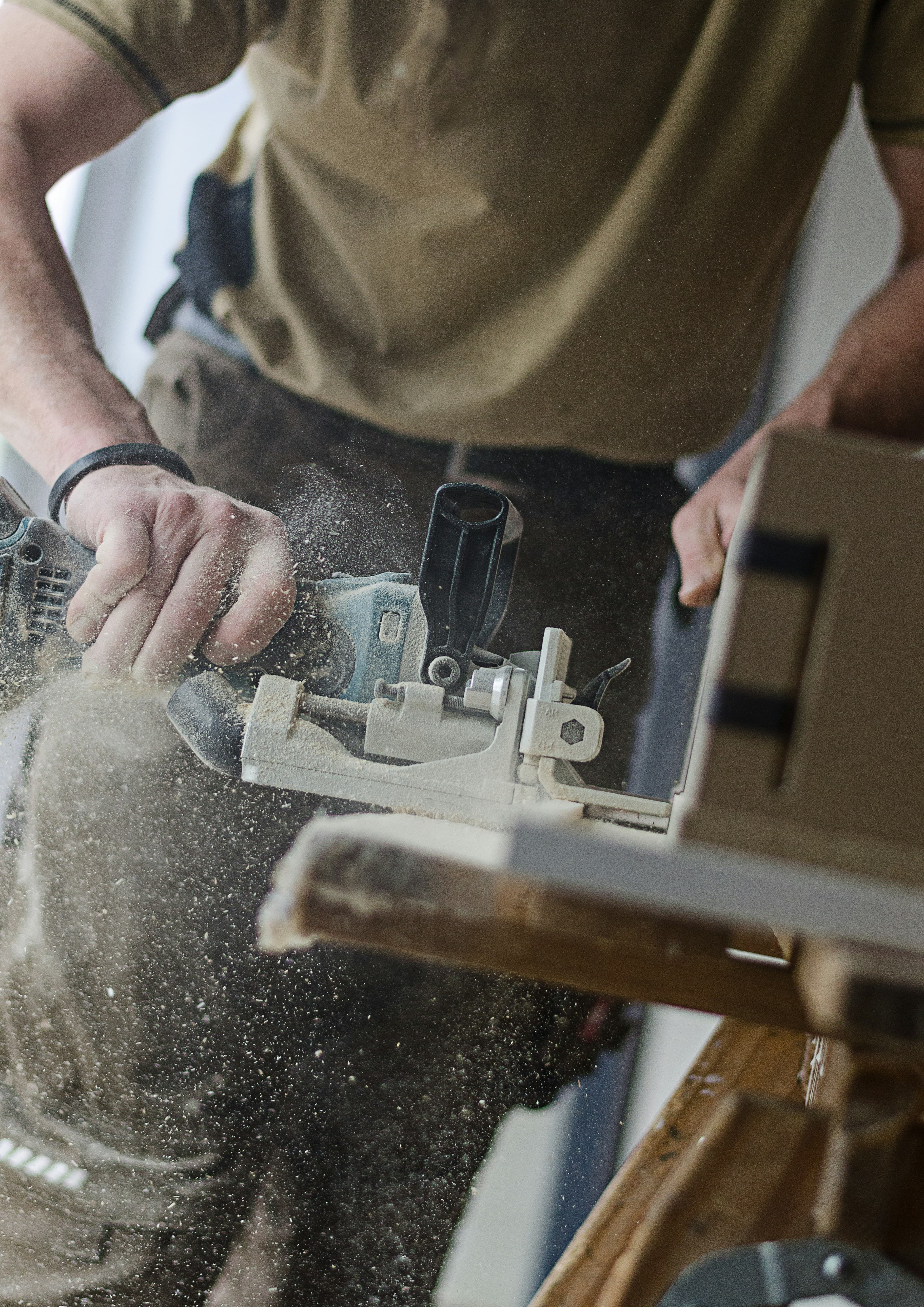 Carpenter cutting timber with a power tool as sawdust flies